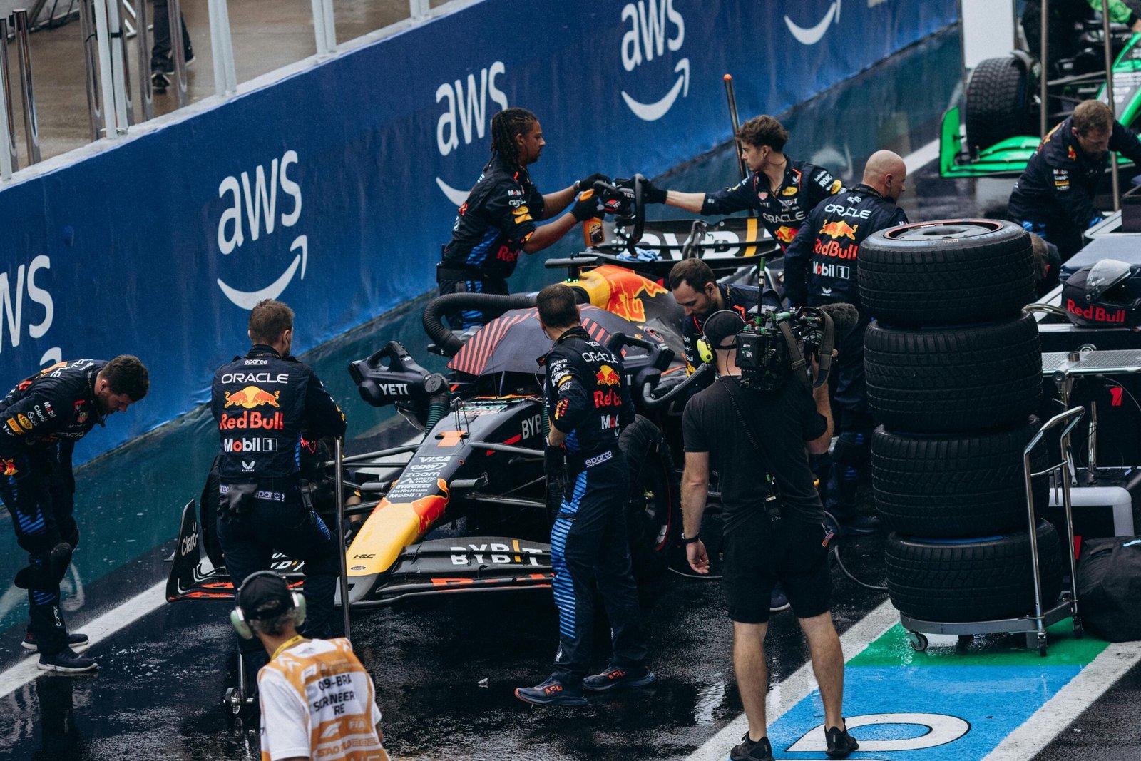 Formula One pit crew servicing the racing car during a pit stop at a wet track.